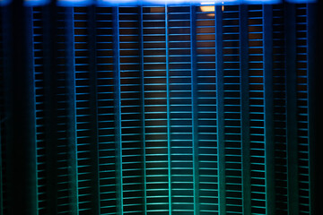 Cool blue light casts shadows on a vented surface in an indoor space, creating an abstract display...