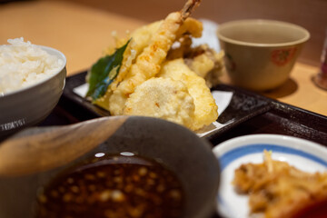 Japanese teishoku meal featuring assorted tempura, including shrimp, vegetables, and mushrooms, served with steamed rice, dipping sauce, and side dishes in a traditional setting