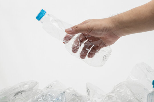 Hand holding crumpled plastic bottle, ready to drop on a pile of plastic bottle waste.