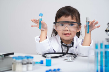 A young child in a lab coat and safety glasses holds test tubes, showcasing curiosity and...