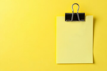 A yellow memo pad clipped by a shiny black paper fastener