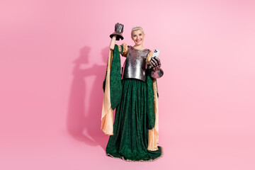 Elegant young woman dressed as a medieval queen holding a phone against a pink background