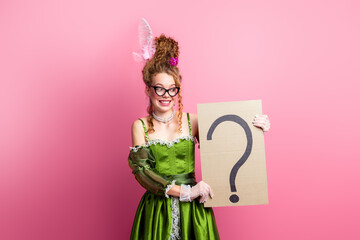 Young woman in green baroque-era costume holding a sign against a vibrant pink background