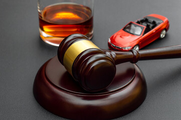 Judge's gavel with toy car and glass of whiskey on black.