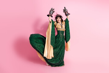 Elegant medieval-themed woman dancing in emerald green and gold costume with pink backdrop