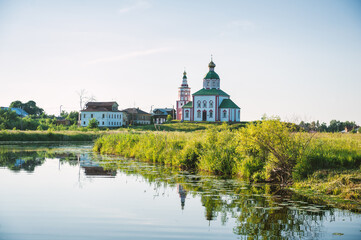 Fototapeta premium Orthodox church with green domes reflected in calm river water.