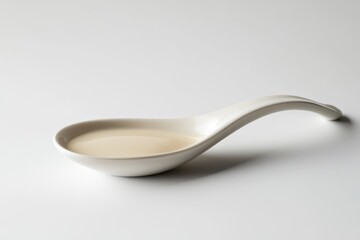 A porcelain spoon holds a small amount of light beige liquid against a white background.