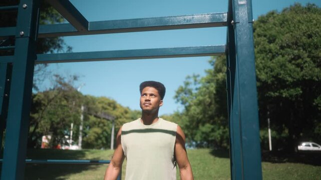 Athletic man walking towards a pull-up bar and starting pull-ups with determination, captured in a natural outdoor park setting