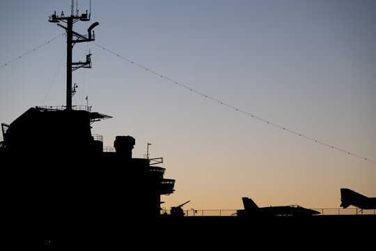 Aircraft carrier silhouette against twilight sky with fighter jets at naval base during evening hours - Powered by Adobe
