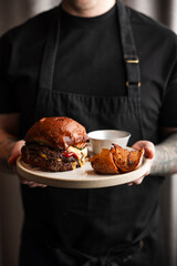 Chef Presenting a Gourmet Cheeseburger with Roasted Potatoes and Sauce

