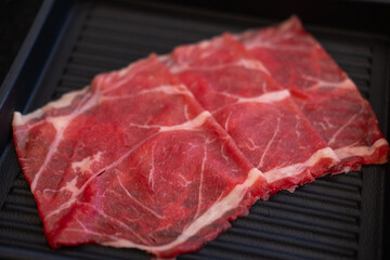 A close-up shot of sliced raw meat, arranged on a plate, ready to be cooked in a hot pot