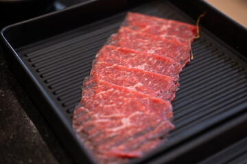 A close-up shot of sliced raw meat, arranged on a plate, ready to be cooked in a hot pot