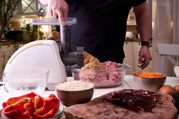 a man chops meat and vegetables in an electric meat grinder to make mincemeat for cutlets