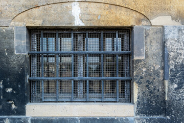 Rectangular basement window with iron grille and steel mesh against an old stone wall. From the series of windows of the world.