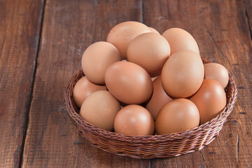 Raw brown eggs arranged in a basket with a rustic wooden background