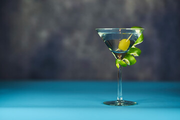 Refreshing Martini glass with green olives inside, on a sky blue and grey surface