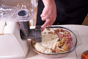 a man chops meat and vegetables in an electric meat grinder to make mincemeat for cutlets