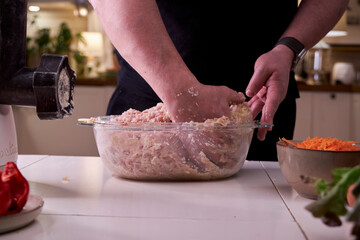 A man mixes dietary minced chicken and vegetables in a glass bowl with his hands
