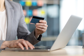 A woman is shopping online using her credit card and laptop in the office, making secure purchases from the comfort of her desk