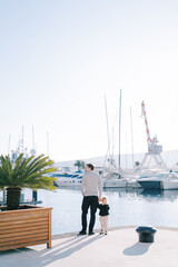 Obraz premium Dad and a little girl are standing on the embankment holding hands. Back view