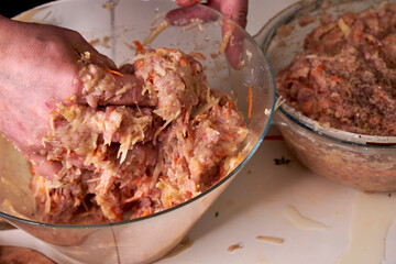 A man mixes dietary minced chicken and vegetables in a glass bowl with his hands