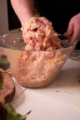 A man mixes dietary minced chicken and vegetables in a glass bowl with his hands