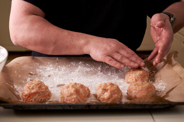 a man molds chicken meatballs and puts them on a baking tray, close up