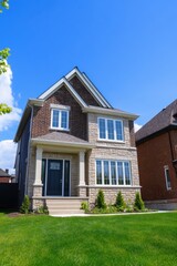 Obraz premium Newly constructed two-story house with brick and stone facade on a sunny day in a suburban neighborhood featuring green lawn and clear blue sky
