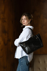 A girl in a white shirt and blue jeans is posing with a black shopper bag.