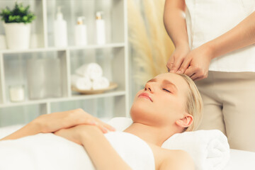 Caucasian woman enjoying relaxing anti-stress head massage and pampering facial beauty skin recreation leisure in dayspa modern light ambient at luxury resort or hotel spa salon. Quiescent