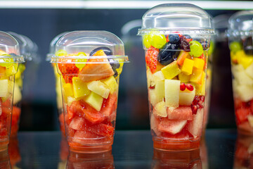 A vibrant photo of fresh fruit cups filled with various colorful fruits, including strawberries, grapes, watermelon, mango, pineapple, and pomegranate seeds. The transparent cups with dome 