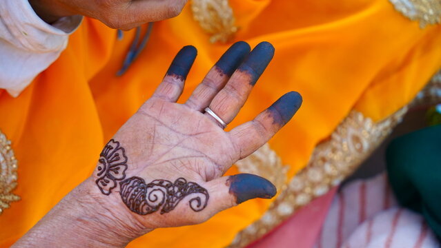 A home artist drawing simple mehandi design on hand. Closeup woman hand applying henna tattoo also known as mehndi, inai, hina, camphire, and hena. Indian old lady's hand. Liquid paste cone