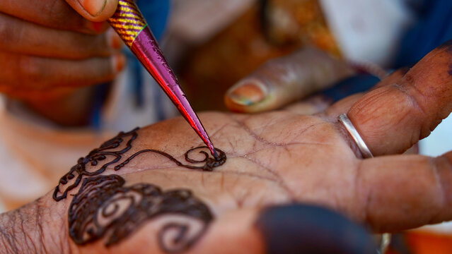 A home artist drawing simple mehandi design on hand. Closeup woman hand applying henna tattoo also known as mehndi, inai, hina, camphire, and hena. Indian old lady's hand. Liquid paste cone