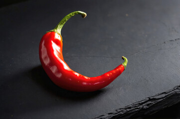 Red chili pepper arched against dark backdrop emphasizes chili intensity. Vivid hue and curved silhouette reflect natural heat, sparking flavor ideas for modern cooking experiments