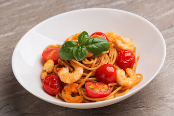 Whole grain spaghetti pasta with shrimp, cherry tomato in a white bowl ready to eat. Mediterranean...