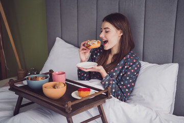 Young woman enjoying breakfast in bed wearing polka dot pajamas, embracing leisure and comfort on a...
