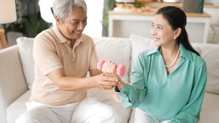 Obraz premium Happy elderly couple exercising together with dumbbells at home, focusing on muscle strength, joint health, and physical wellness for improved mobility and healthy aging. Retirement concept. Myrmidon.