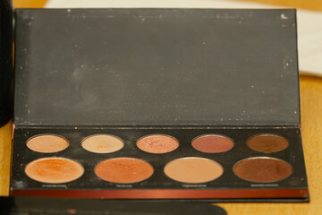 A makeup brush picks up powder from a contour palette, featuring various warm shades. A...