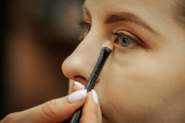 close-up of a woman applying makeup under her eye with a soft brush. Her blue eyes and well-groomed eyebrows enhance the beauty focus.
