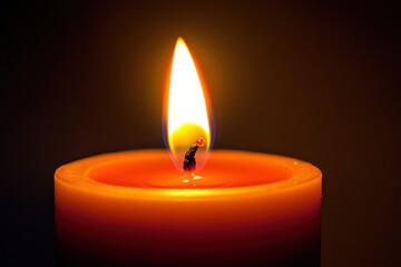 A burning flame atop an orange wax candle glowing brightly