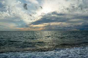Fototapeta premium The sound of sea waves crashing on a pebble beach. The setting sun hid behind dark clouds.