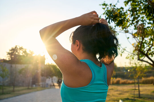 Young Latin sportswoman tying hair with glucose sensor or monitor at sunset in park