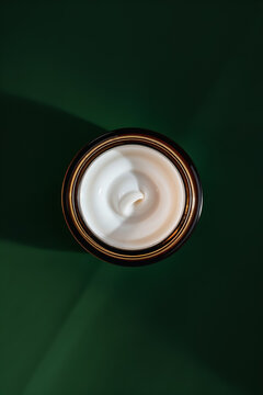 Brown glass jar with white face cream. Whipped beef tallow facial moisturizer photographed from in flat lay style on green leaf