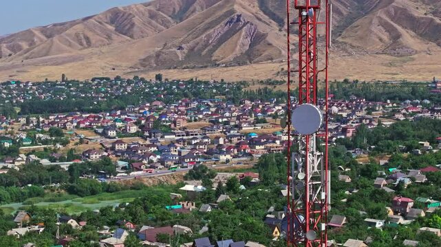 Drone footage showing a mountain village near with a telecom tower on a dry hill. The drone flying slowly in an arc around the tower, creating a parallax effect with distant foothill in the background