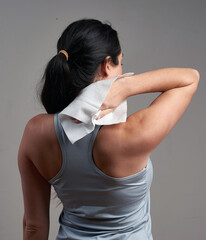 A woman in athletic wear wipes the back of her neck with a disposable wipe or towel, possibly after...