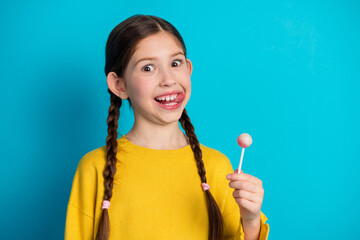 Adorable young girl enjoying a candy treat against a vibrant blue background, expressing happiness and playfulness