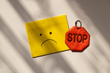 Yellow paper with sadness drawn on it and reflective sign with stop text on white background with...