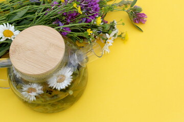 There is a teapot with chamomile infusion on a yellow background.	