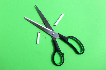 On a green background lie large scissors and a cigarette cut in half.