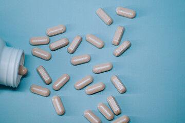 Supplement pills spill on light blue surface, showing various shapes and sizes scattered around